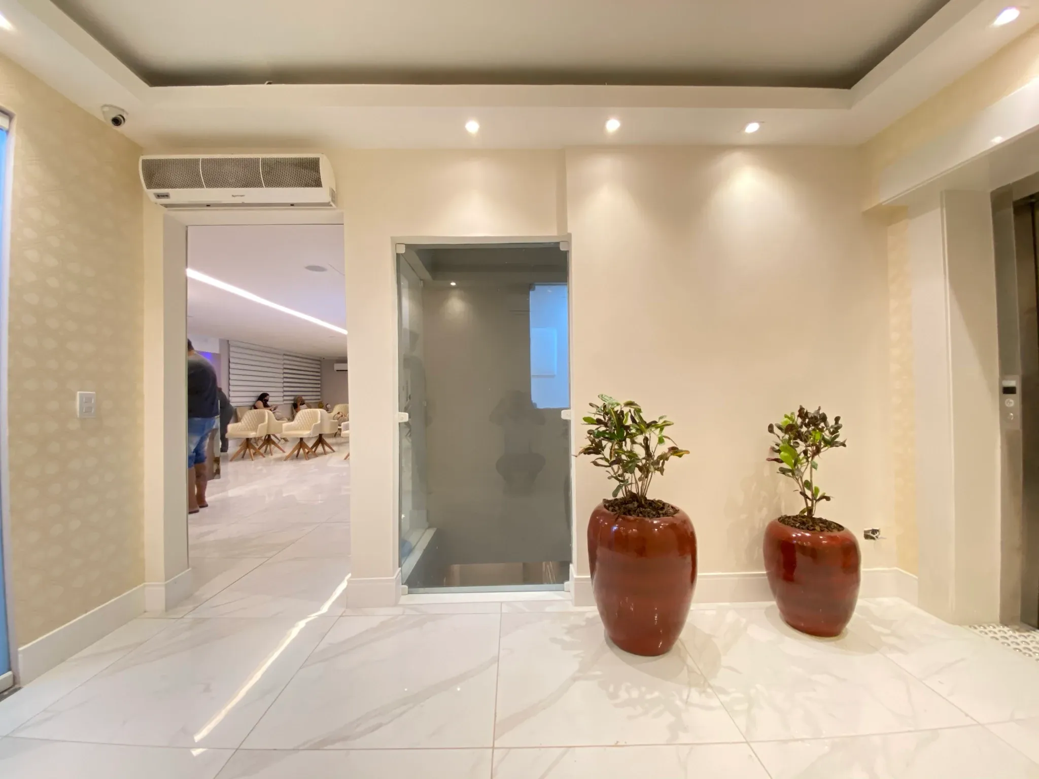 Hall dos elevadores e antecâmara de entrada com piso em porcelanato marmorizado polido, papel de parede dourado, vasos vietnamitas conhaque e vista para a sala de espera