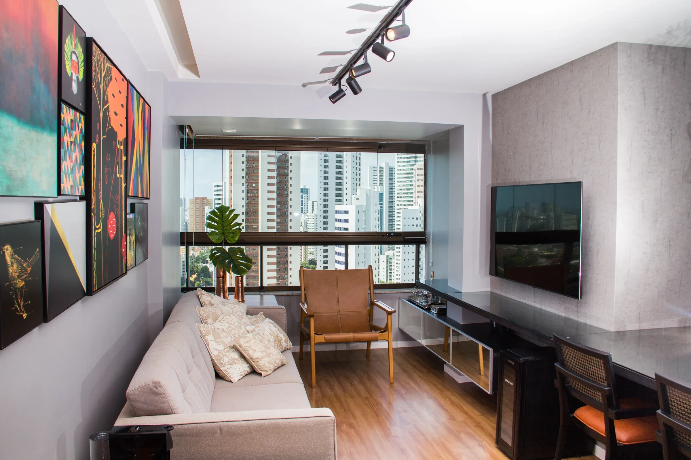 Sala de estar com painel de TV em acabamento cimento queimado, rack com portas espelhadas bronze, adega climatizada embutida e iluminação por trilhos de spots pretos