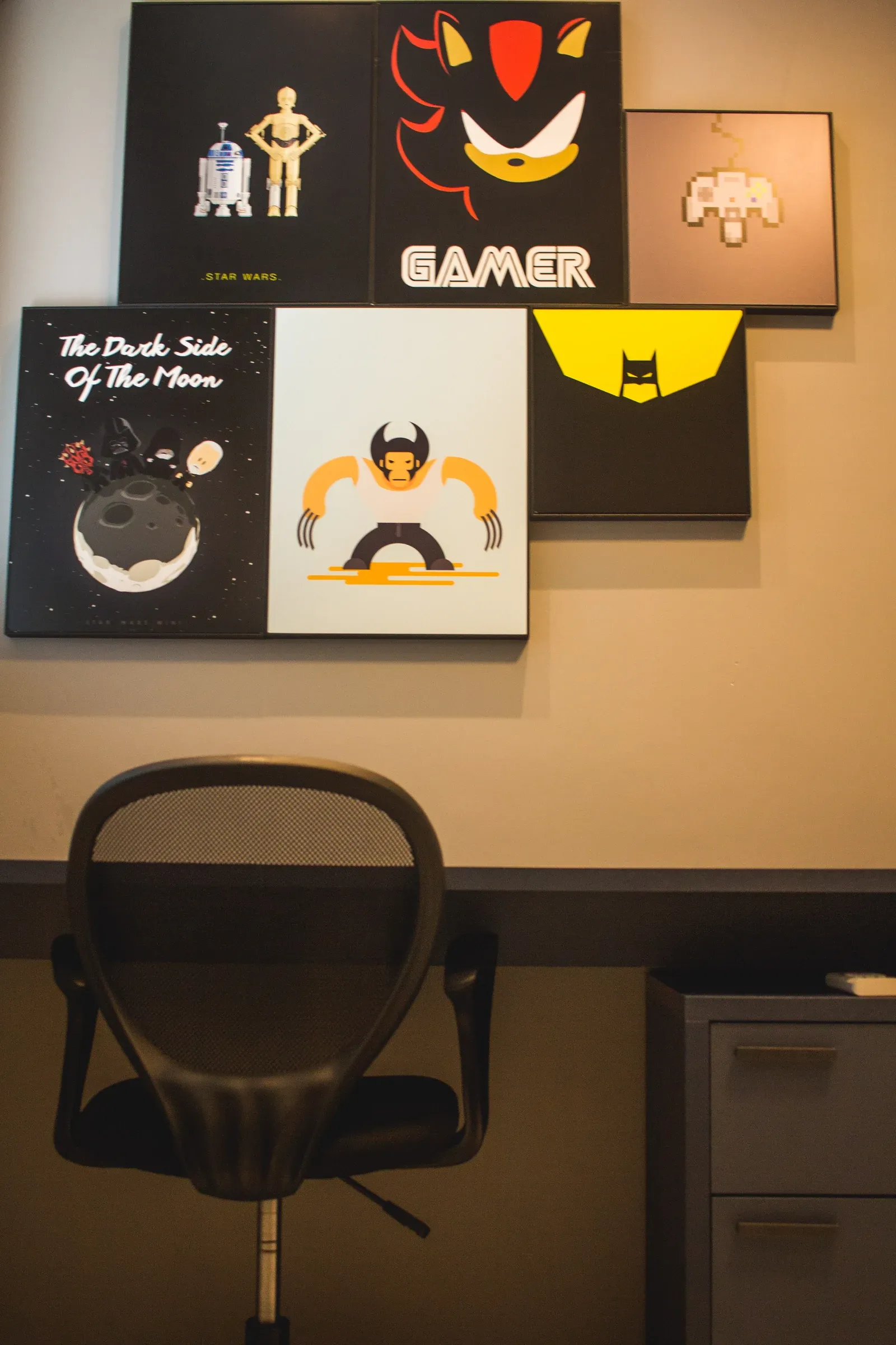 Estação de trabalho e estudos com cadeira giratória mesh preta e composição de quadros temáticos pop/gamer na parede cinza