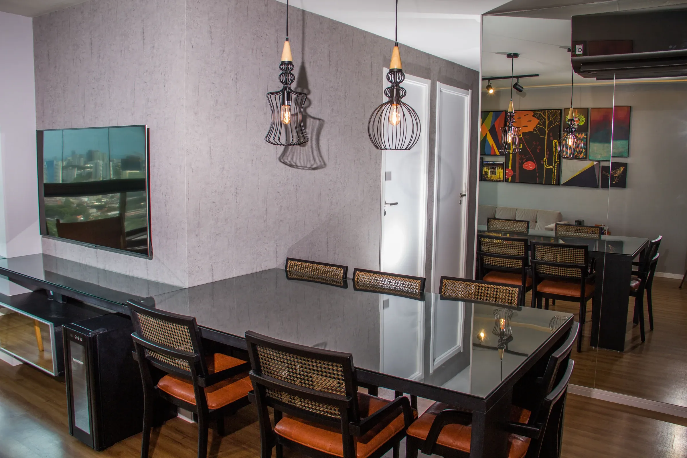 Sala de jantar com mesa de tampo em vidro preto, cadeiras com encosto em palhinha e assento em couro caramelo, espelho amplo e pendentes geométricos aramados