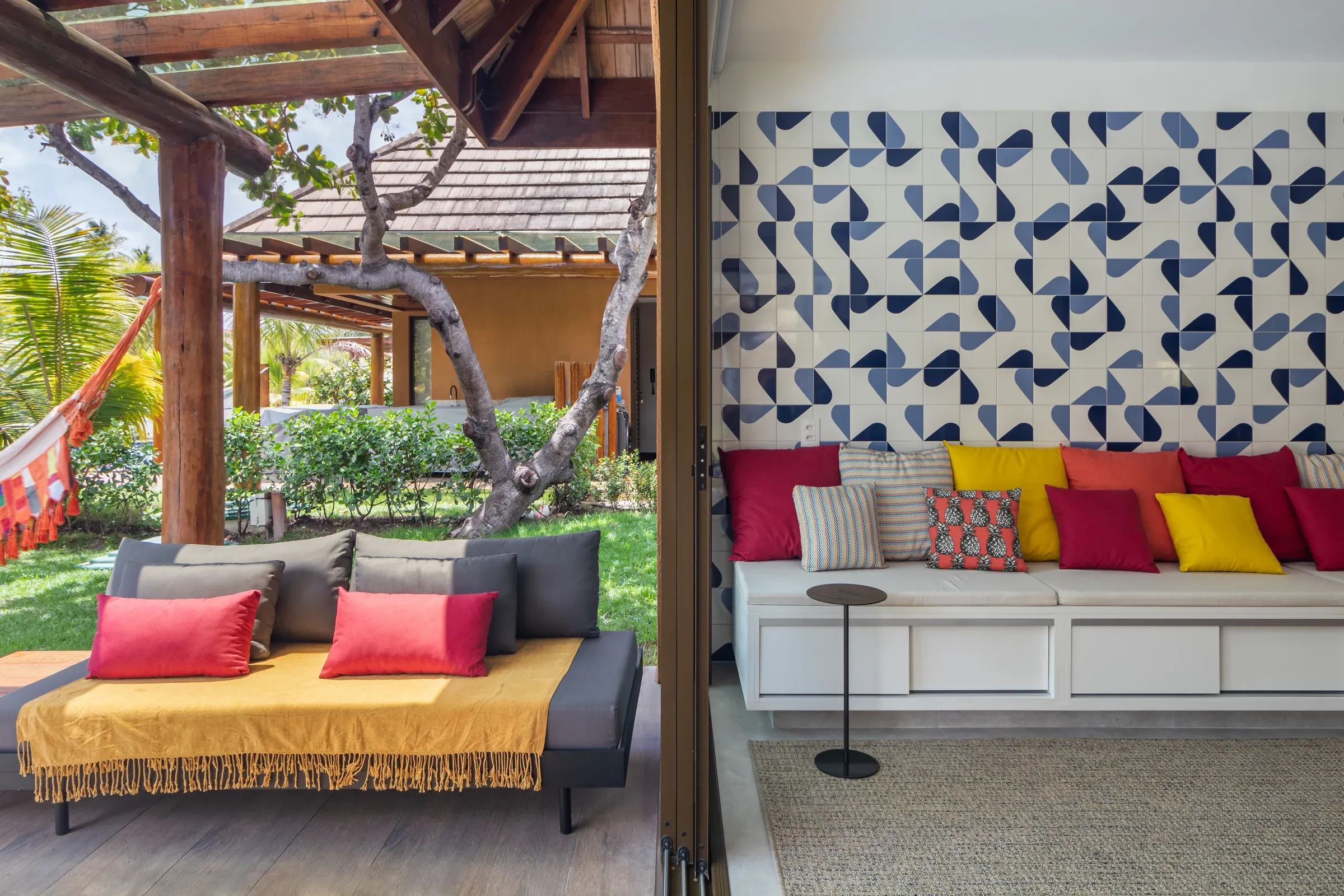 Integração entre sala de estar e terraço gourmet, com painel de azulejos geométricos azuis e brancos, banco em alvenaria e daybed sob pergolado