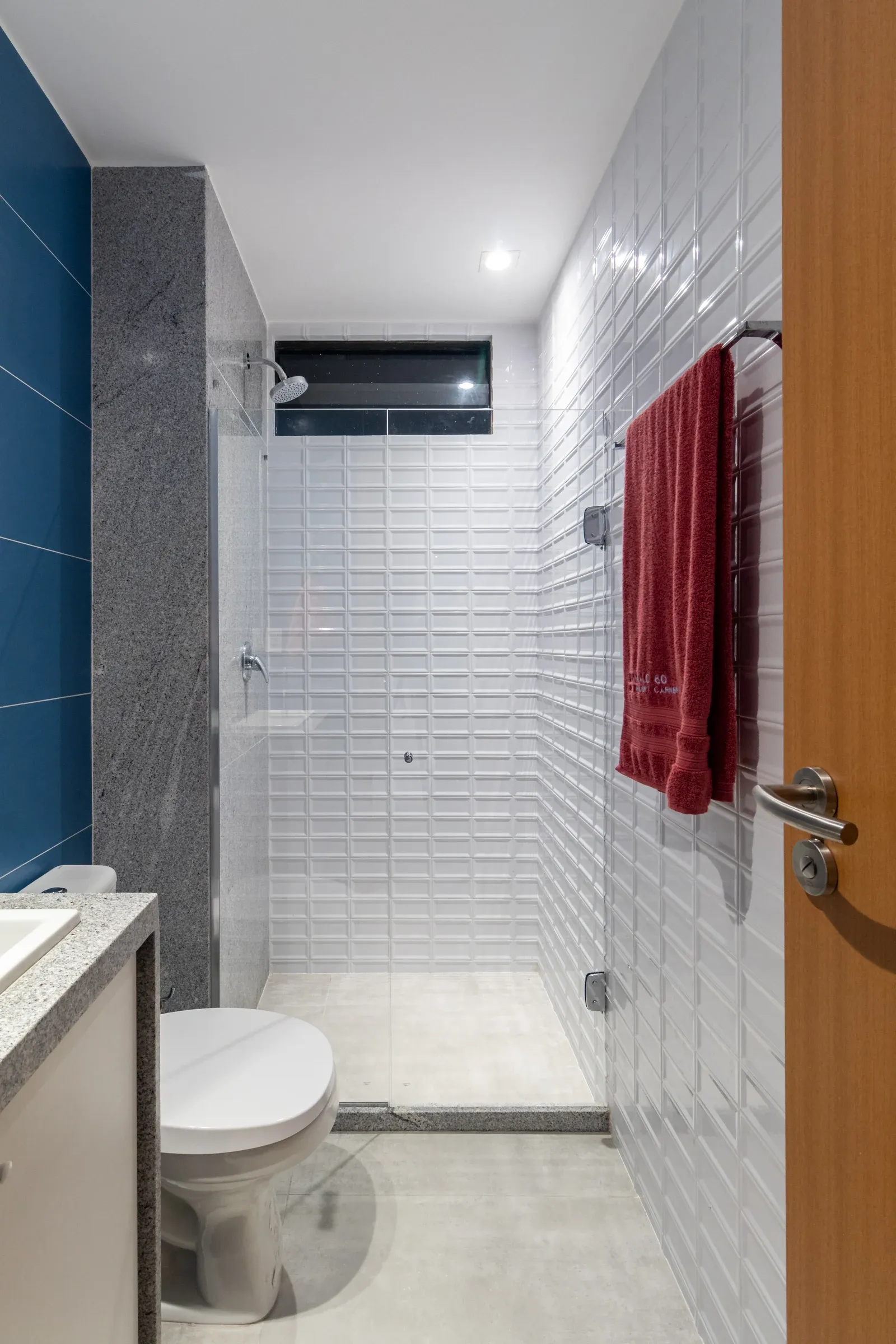Banheiro contemporâneo com revestimento em tijolinhos de metrô brancos bisotados no box, parede azul de destaque e bancada em granito cinza
